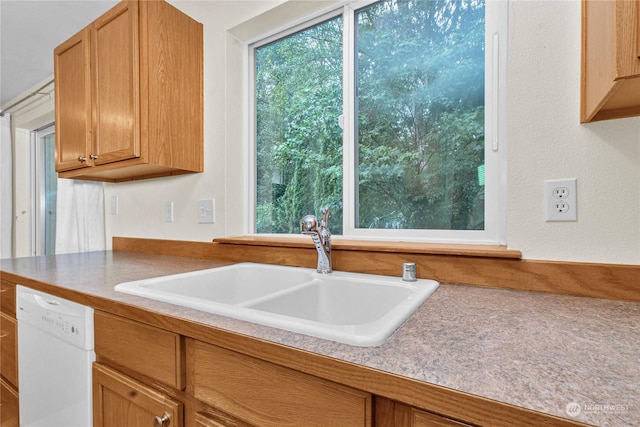 kitchen with light countertops, white dishwasher, a sink, and brown cabinets