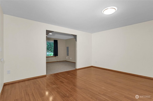 unfurnished room featuring electric panel, baseboards, arched walkways, and wood finished floors