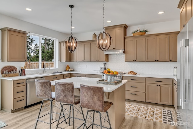 kitchen with premium appliances, sink, pendant lighting, light hardwood / wood-style flooring, and a kitchen island