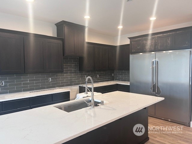 kitchen with light stone countertops, light wood-type flooring, tasteful backsplash, high quality fridge, and sink