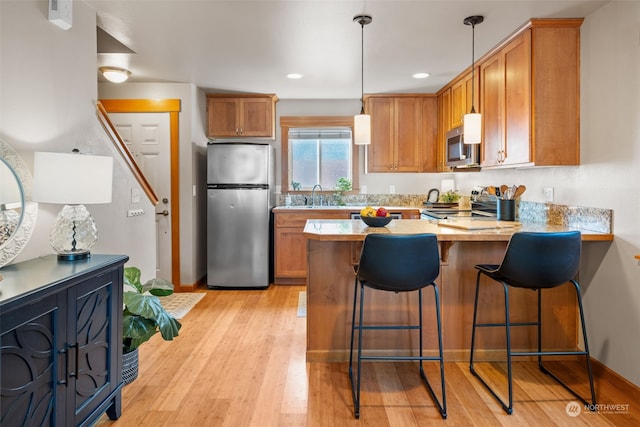 kitchen with light hardwood / wood-style flooring, appliances with stainless steel finishes, sink, kitchen peninsula, and a breakfast bar area