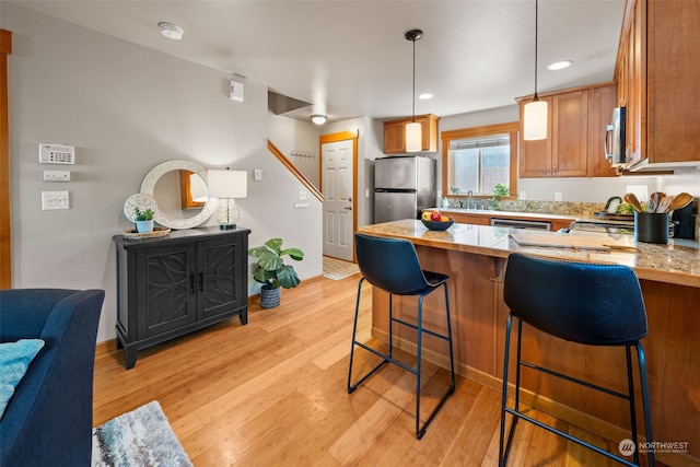 kitchen with stainless steel appliances, light hardwood / wood-style floors, kitchen peninsula, pendant lighting, and a kitchen bar