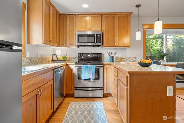 kitchen with decorative light fixtures, appliances with stainless steel finishes, sink, and light hardwood / wood-style flooring