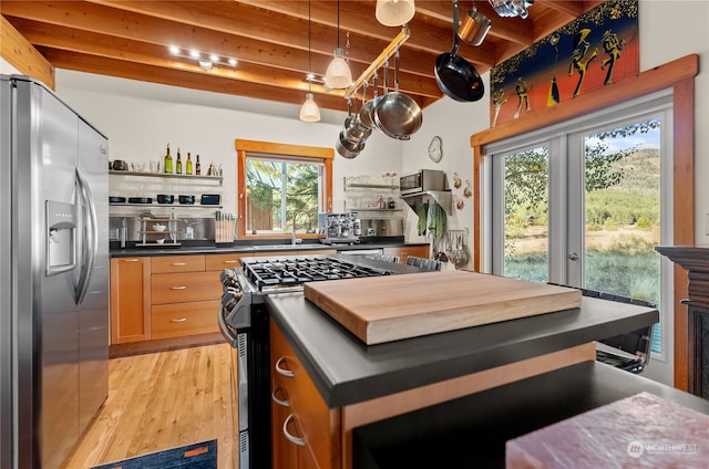 kitchen with beamed ceiling, appliances with stainless steel finishes, sink, and light wood-type flooring