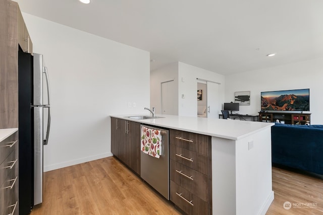 kitchen with light wood-type flooring, stainless steel appliances, kitchen peninsula, sink, and dark brown cabinetry