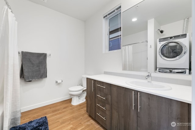 bathroom featuring curtained shower, hardwood / wood-style flooring, toilet, stacked washer / dryer, and vanity