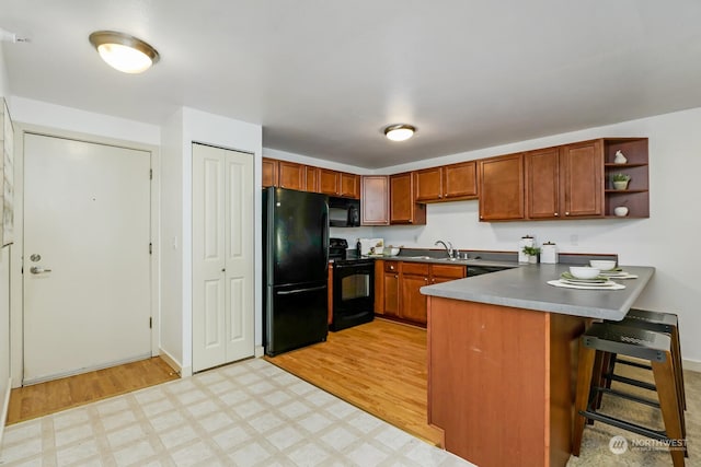 kitchen with brown cabinetry, light floors, a peninsula, black appliances, and open shelves