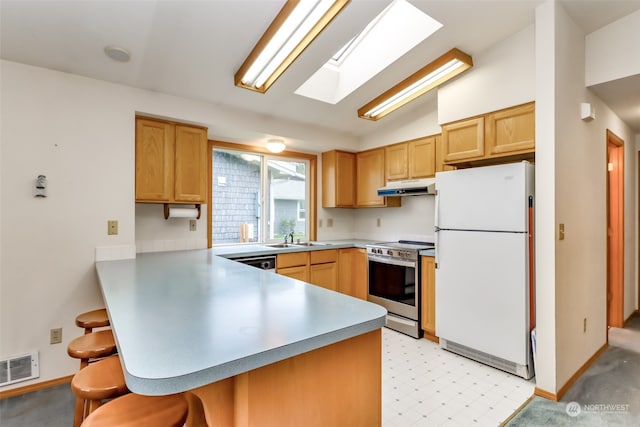 kitchen featuring a breakfast bar area, white fridge, vaulted ceiling with skylight, sink, and stainless steel range