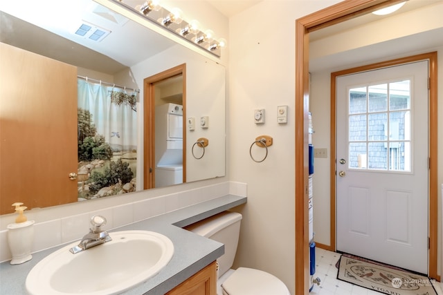 bathroom featuring stacked washer / dryer, vanity, and toilet