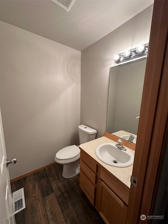 half bath with vanity, wood finished floors, visible vents, a textured ceiling, and toilet