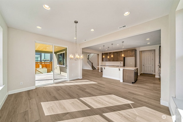 kitchen with tasteful backsplash, a center island with sink, a chandelier, light hardwood / wood-style floors, and decorative light fixtures