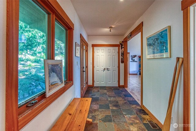 corridor with stone finish floor, baseboards, and visible vents
