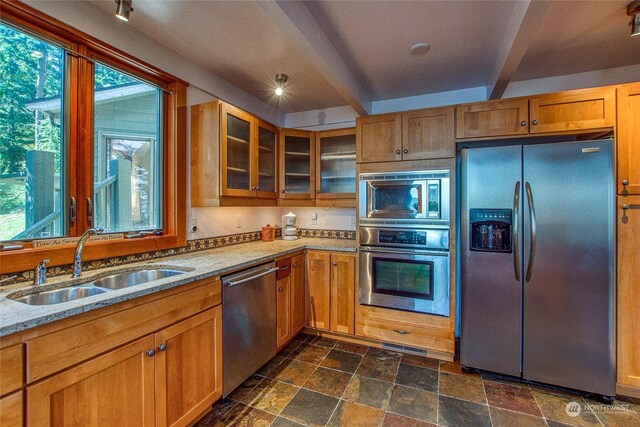 kitchen with stainless steel appliances, light stone countertops, a sink, and a healthy amount of sunlight