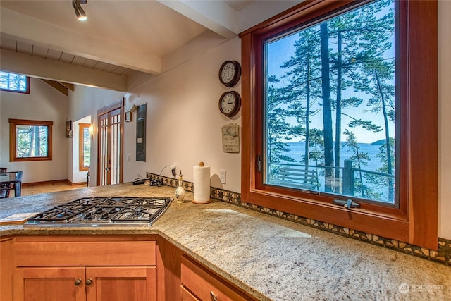 kitchen with lofted ceiling with beams, a peninsula, brown cabinets, stainless steel gas cooktop, and light stone counters