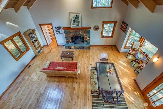 living area featuring high vaulted ceiling, wood-type flooring, a stone fireplace, and a healthy amount of sunlight