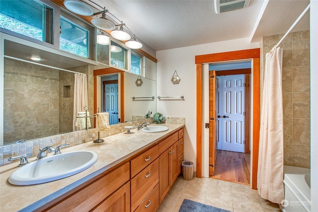 full bathroom featuring double vanity, visible vents, a textured ceiling, and a sink