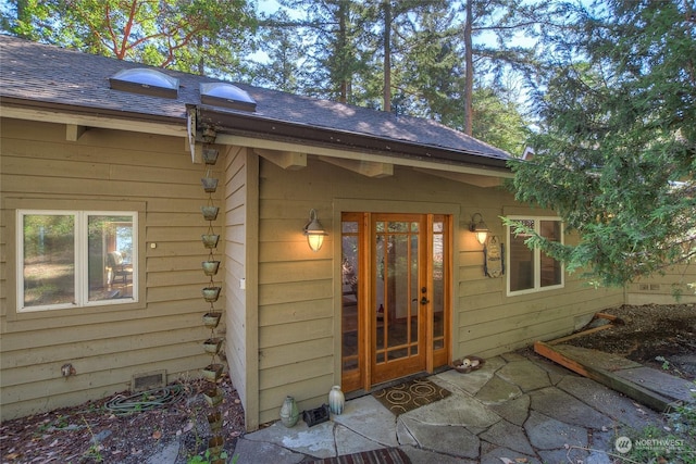 entrance to property featuring roof with shingles and a patio area