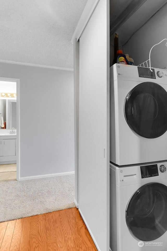 washroom with a textured ceiling, light hardwood / wood-style flooring, ornamental molding, sink, and stacked washer / dryer