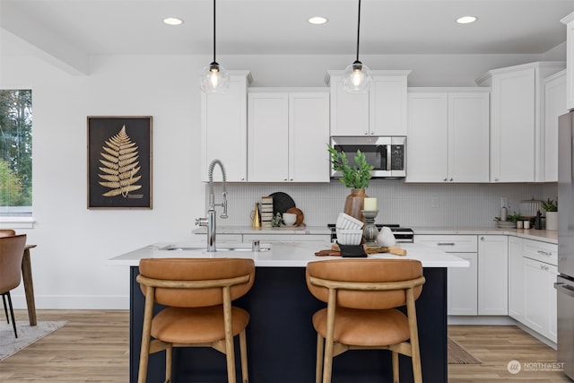 kitchen featuring decorative light fixtures, light hardwood / wood-style floors, an island with sink, and white cabinets