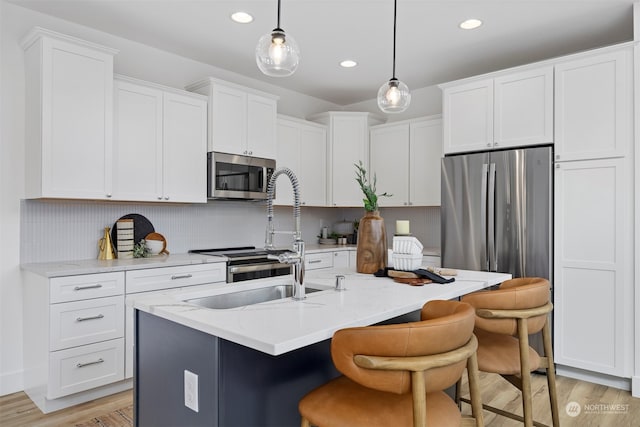 kitchen with an island with sink, light stone countertops, stainless steel appliances, light hardwood / wood-style flooring, and decorative light fixtures