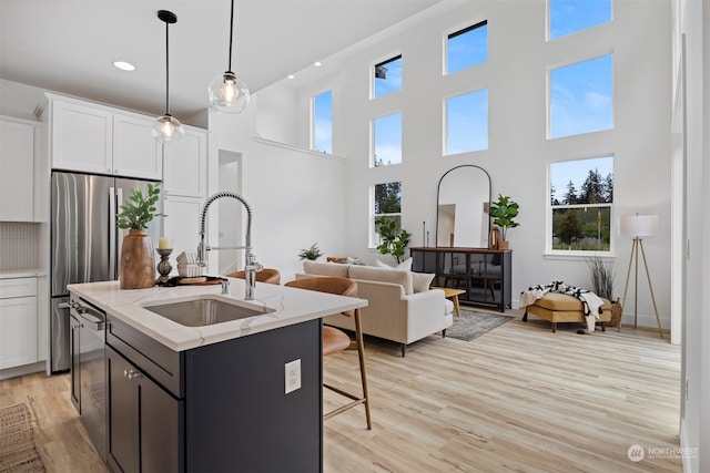 kitchen with white cabinets, hanging light fixtures, sink, a kitchen island with sink, and light stone countertops