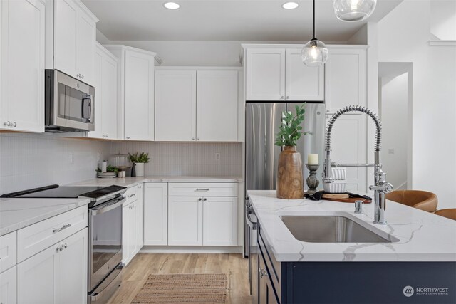 kitchen featuring pendant lighting, white cabinetry, appliances with stainless steel finishes, and light hardwood / wood-style flooring