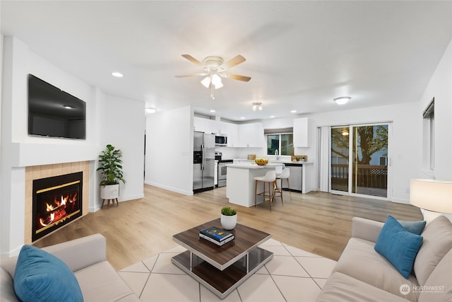 living room with ceiling fan, light hardwood / wood-style floors, sink, and a fireplace