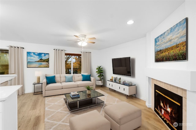 living room with ceiling fan, light hardwood / wood-style floors, and a tiled fireplace