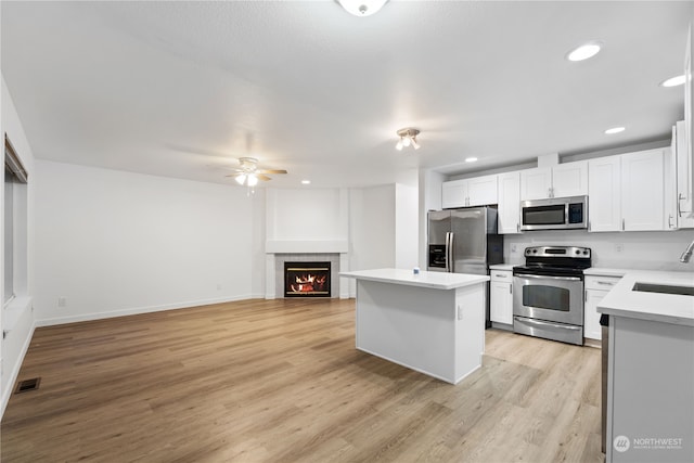 kitchen with a kitchen island, light hardwood / wood-style floors, a fireplace, white cabinets, and appliances with stainless steel finishes