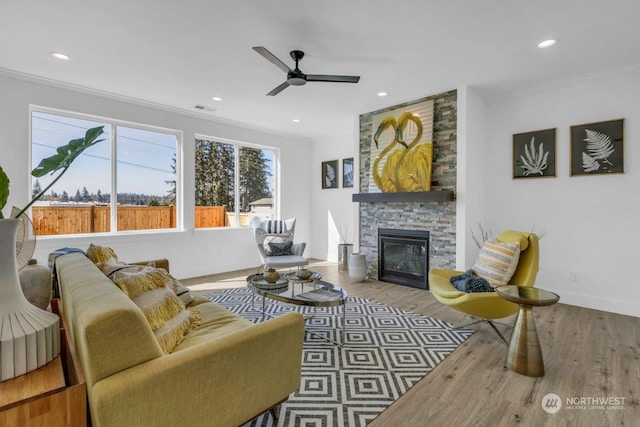 living room with a stone fireplace, ceiling fan, hardwood / wood-style floors, and ornamental molding