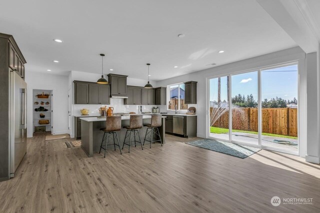 kitchen with a center island, a breakfast bar, light wood-type flooring, appliances with stainless steel finishes, and decorative light fixtures