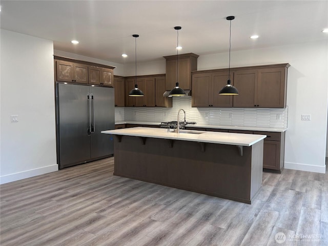 kitchen with a sink, backsplash, high end refrigerator, and light countertops