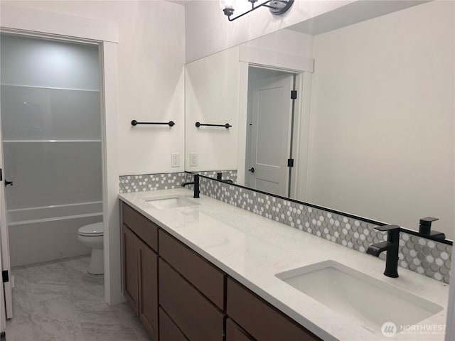 bathroom featuring double vanity, marble finish floor, toilet, and a sink