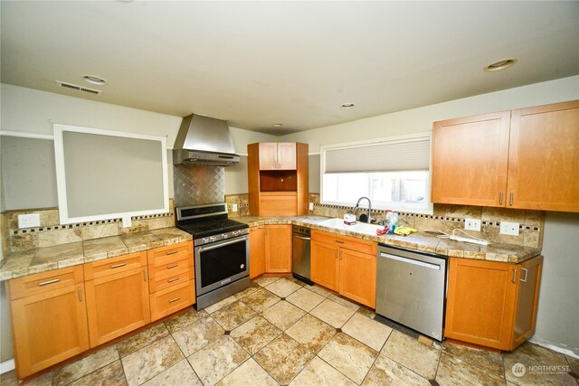 kitchen featuring wall chimney exhaust hood, sink, appliances with stainless steel finishes, and tasteful backsplash