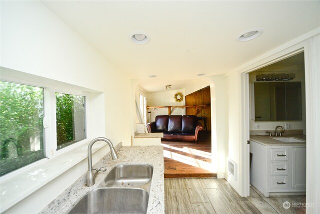 kitchen featuring sink, light stone counters, vaulted ceiling, and light wood-type flooring