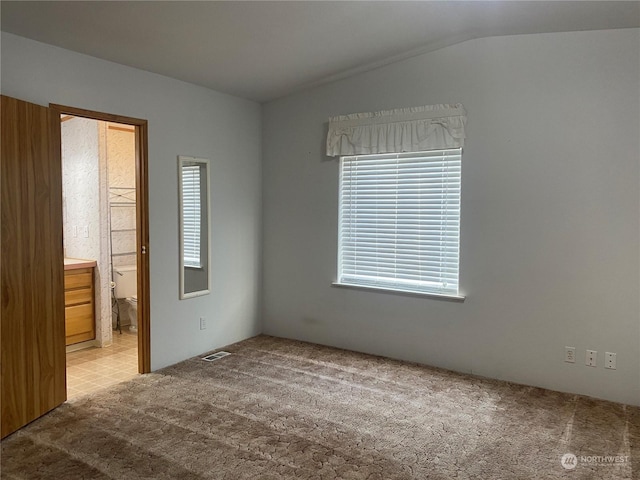 unfurnished bedroom featuring ensuite bath, vaulted ceiling, and light carpet