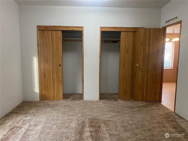 unfurnished bedroom featuring carpet, visible vents, and two closets