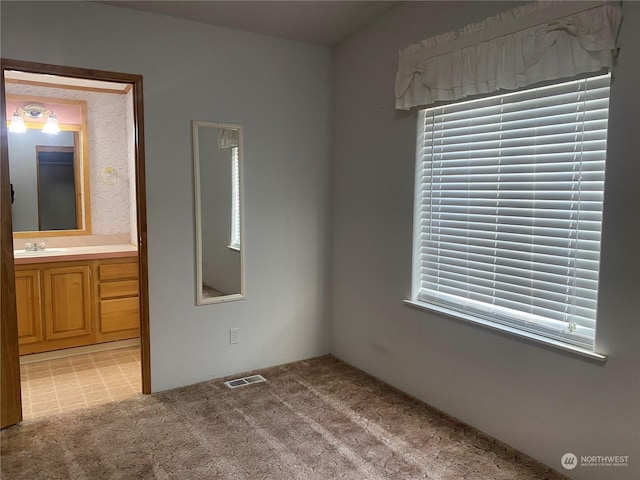 unfurnished bedroom featuring light carpet, multiple windows, visible vents, and a sink