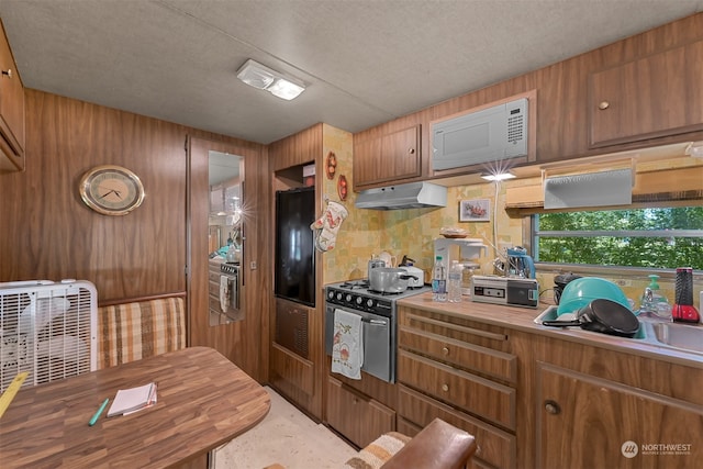 kitchen featuring black fridge, stainless steel gas range, white microwave, and a textured ceiling