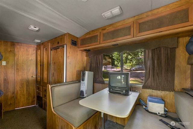 carpeted home office with wooden walls, radiator, and vaulted ceiling