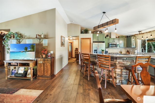 kitchen featuring high vaulted ceiling, stainless steel appliances, green cabinetry, dark hardwood / wood-style flooring, and decorative backsplash