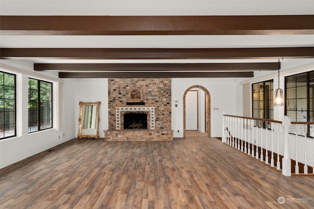 unfurnished living room with a fireplace, beamed ceiling, and wood-type flooring