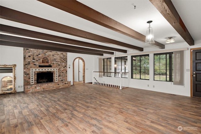 unfurnished living room with wood-type flooring, a brick fireplace, and beam ceiling