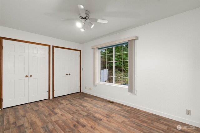 unfurnished bedroom featuring multiple closets, ceiling fan, and dark hardwood / wood-style floors