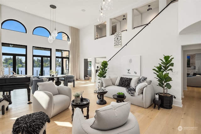 living room with light hardwood / wood-style flooring, a high ceiling, an inviting chandelier, and a water view