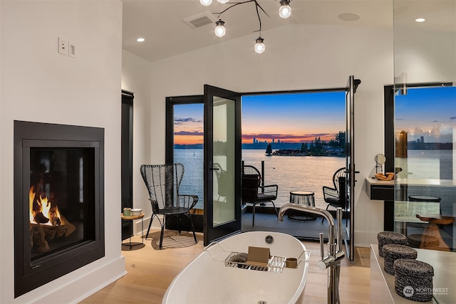 interior space featuring lofted ceiling, hardwood / wood-style floors, a tub to relax in, and a water view