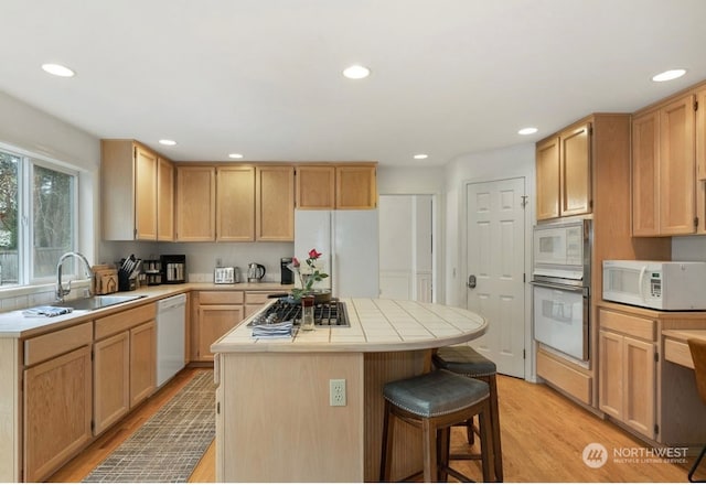 kitchen featuring white appliances, light hardwood / wood-style flooring, a kitchen bar, tile countertops, and a kitchen island