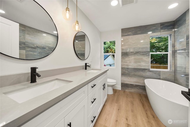 bathroom featuring visible vents, a sink, a freestanding bath, and wood finished floors