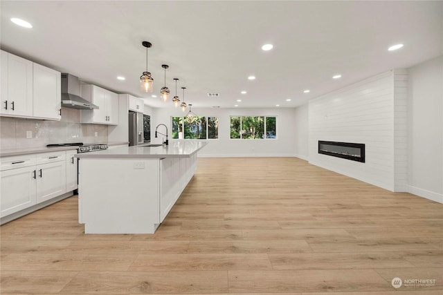 kitchen featuring stainless steel appliances, tasteful backsplash, a large fireplace, a sink, and wall chimney range hood