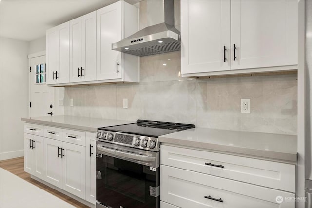 kitchen with wall chimney exhaust hood, light countertops, white cabinetry, and electric stove